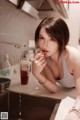 A woman in a white tank top sitting at a kitchen sink.