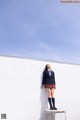 A woman in a school uniform leaning against a white wall.