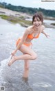 A woman in an orange bikini is standing in the water.