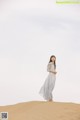 A woman in a long white dress standing on a sand dune.