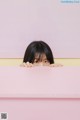 A woman peeking over a pink table with her hands on it.