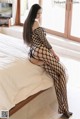 A woman in a black fishnet bodystocking sitting on a bed.