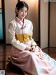 A woman in a pink and white hanbok sitting on the floor.