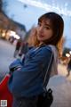 A woman in a denim jacket is holding a shopping bag.