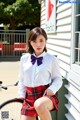 A woman in a white shirt and red plaid skirt posing next to a bicycle.