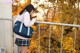 A woman in a school uniform leaning against a railing.