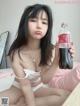 A woman sitting on a bed holding a bottle of coke.