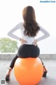 A woman sitting on an orange ball with her back to the camera.