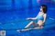 A woman in a blue bikini sitting on the edge of a swimming pool.