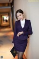 A woman in a purple suit leaning against a wall.