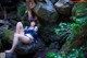 A woman tied up to a rock in the woods.