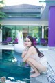 A woman sitting on the edge of a swimming pool next to a house.