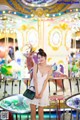 A woman in a white dress standing in front of a carousel.