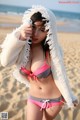 A woman in a bikini on the beach with a towel over her head.