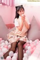 A woman sitting on top of a bed covered in pink and white balloons.