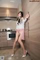 A woman in a white shirt and pink skirt posing in a kitchen.